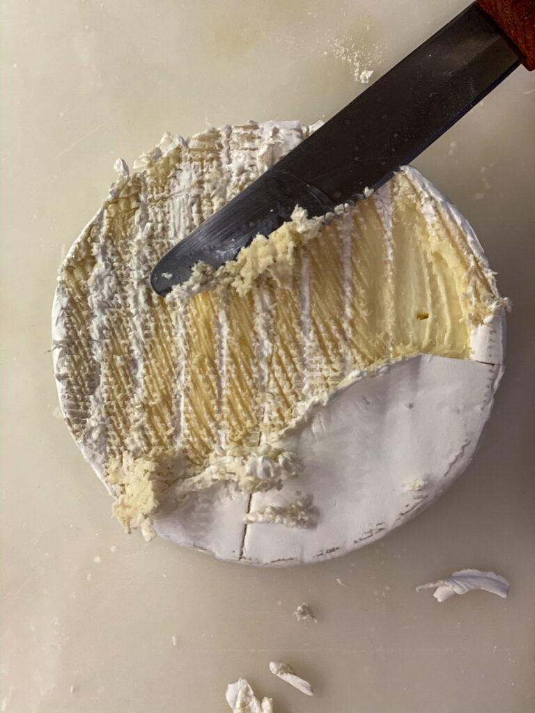 Knife scraping rind off of brie