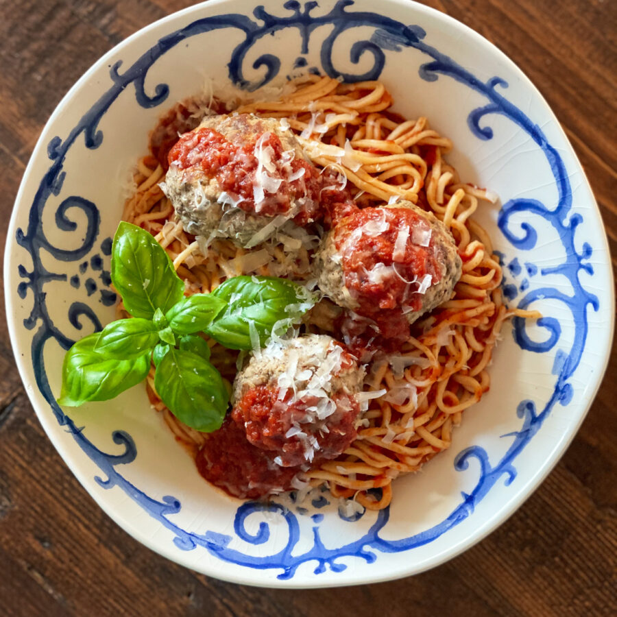 3 MEATBALLS on spaghetti and sauce in a blue and white bowl with basil