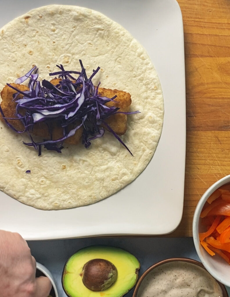 Shredded purple cabbage over a fish stick on a flour tortilla