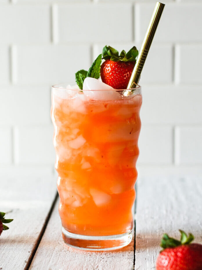 Strawberry moscow mule over ice with a straw and strawberry and mint leaves on top