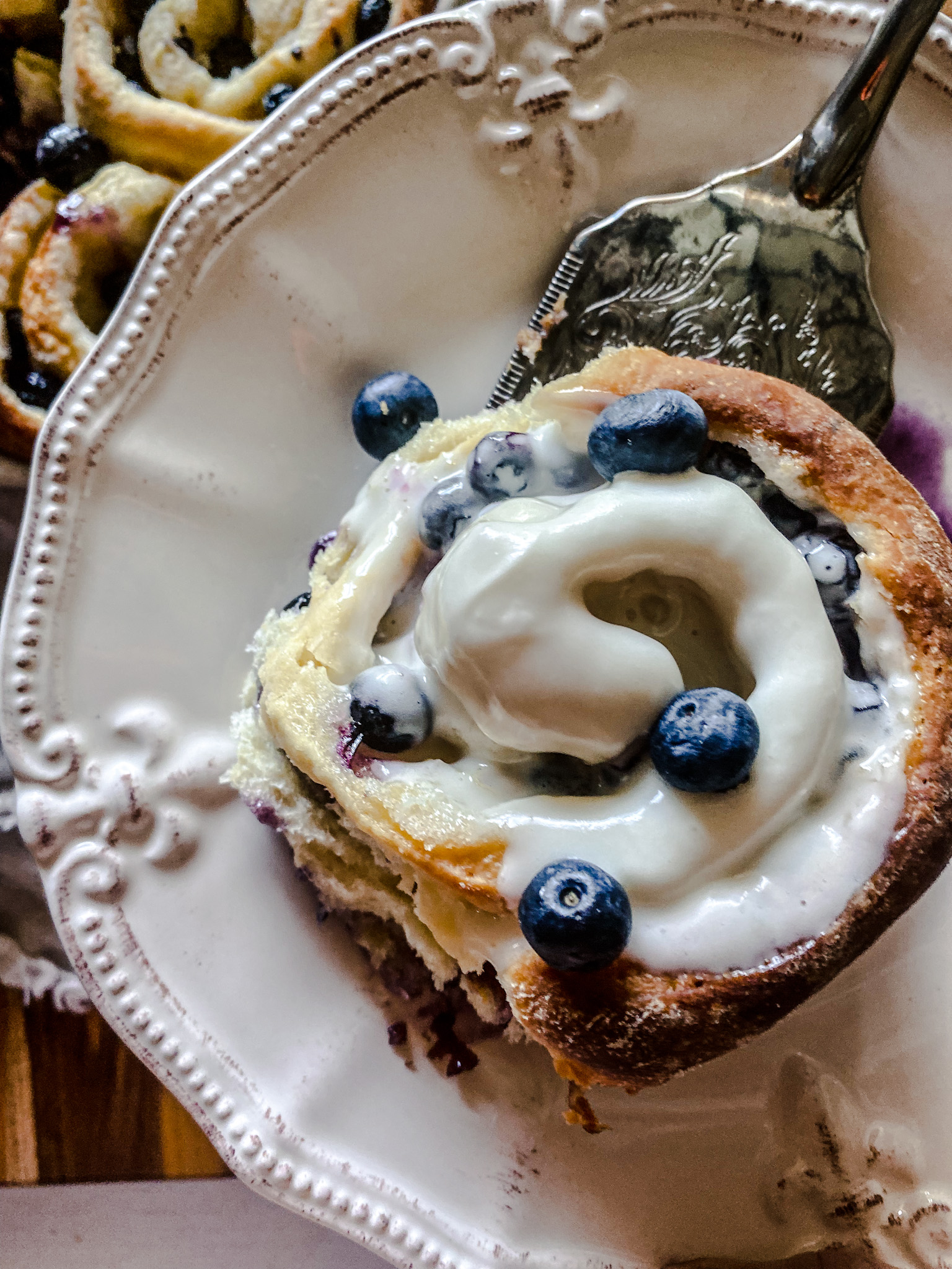 blueberry sweet roll with lemon cream cheese frosting being served onto a white plate