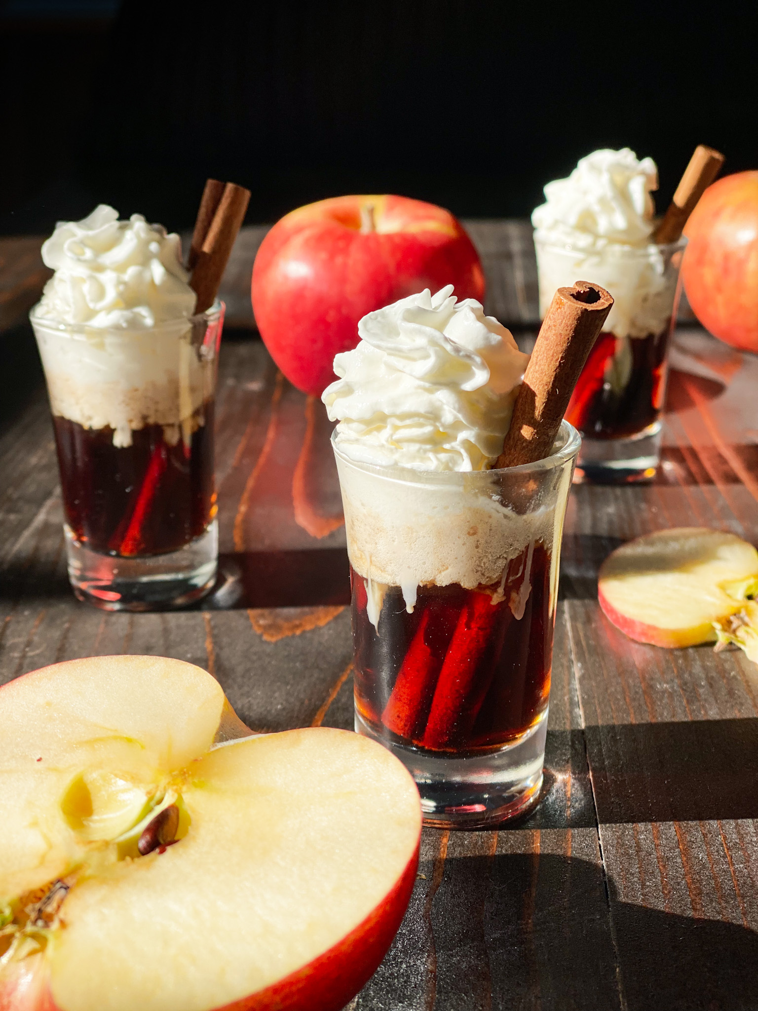 Apple Cinnamon Bourbon shots with whip cream and apples with one sliced