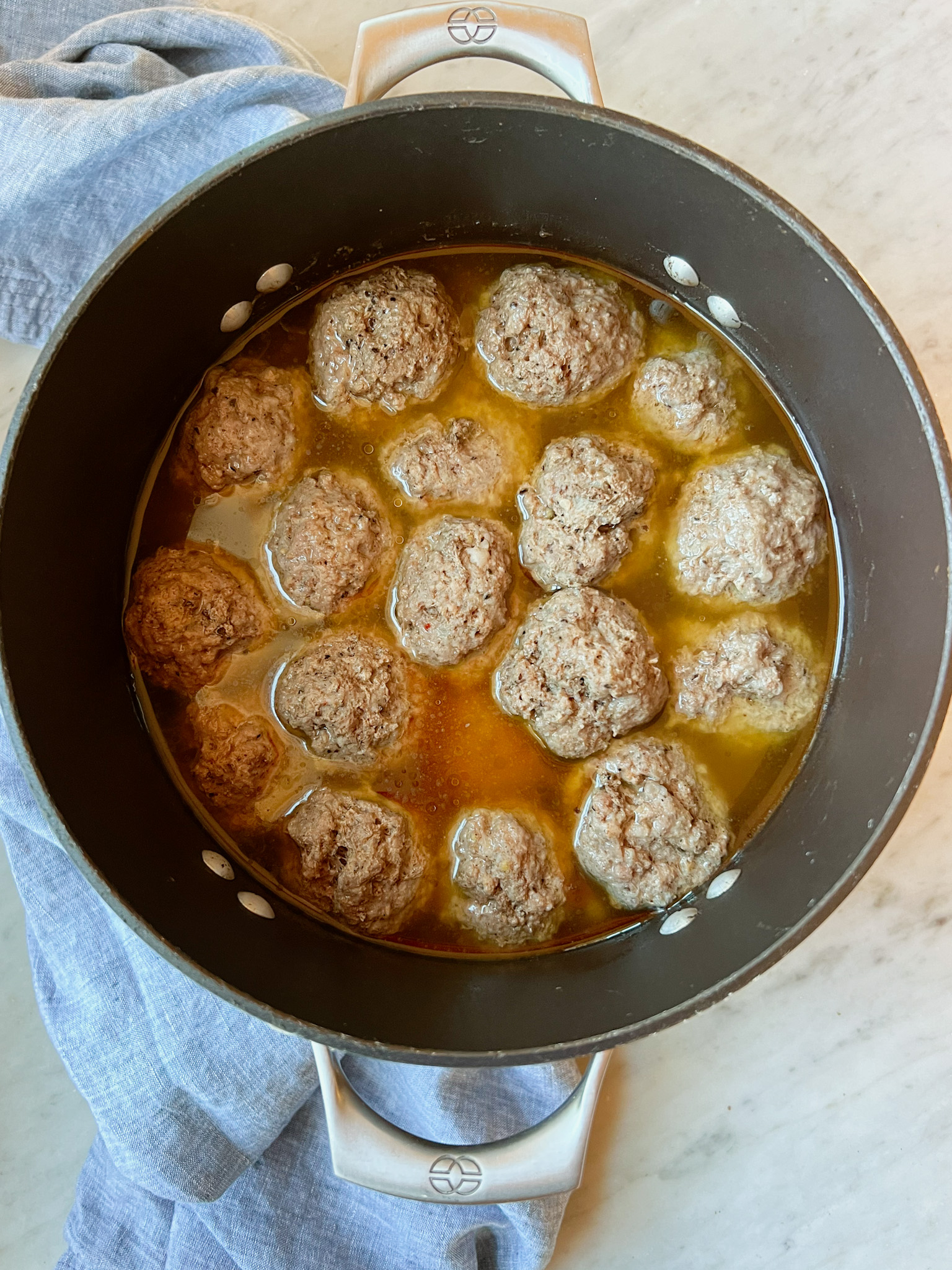 cooked meatballs in broth in a pot with a blue napkin.