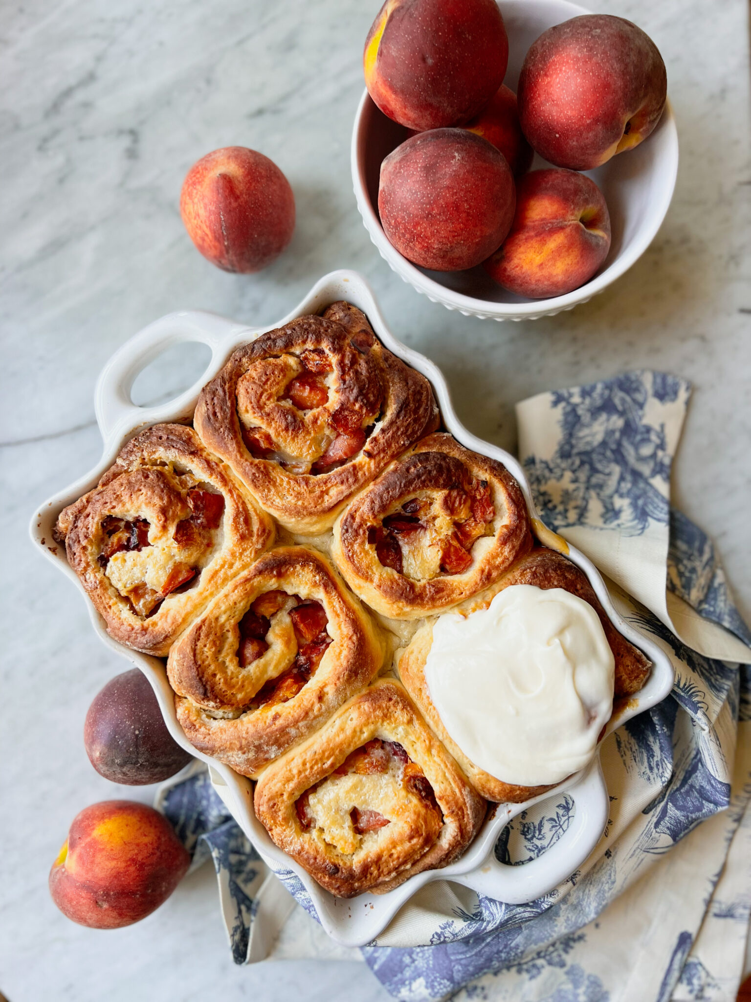 peach rolls with cream cheese frosting and a bowl of peaches