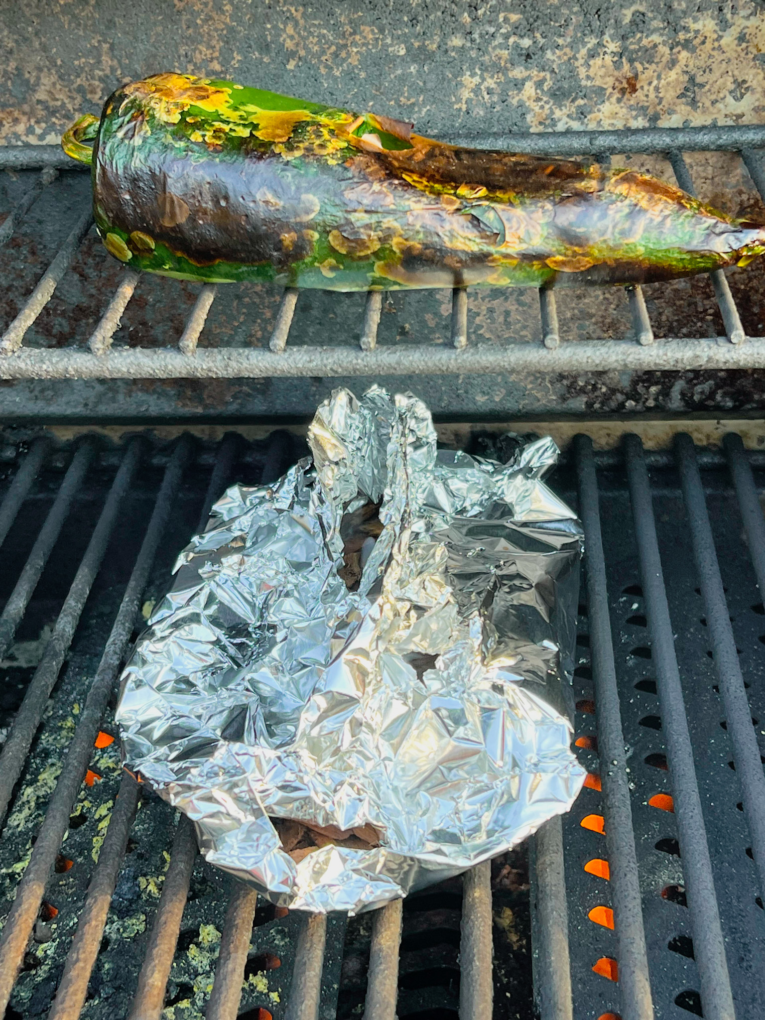 poblano pepper smoking on a grill over a foil package of wood chips