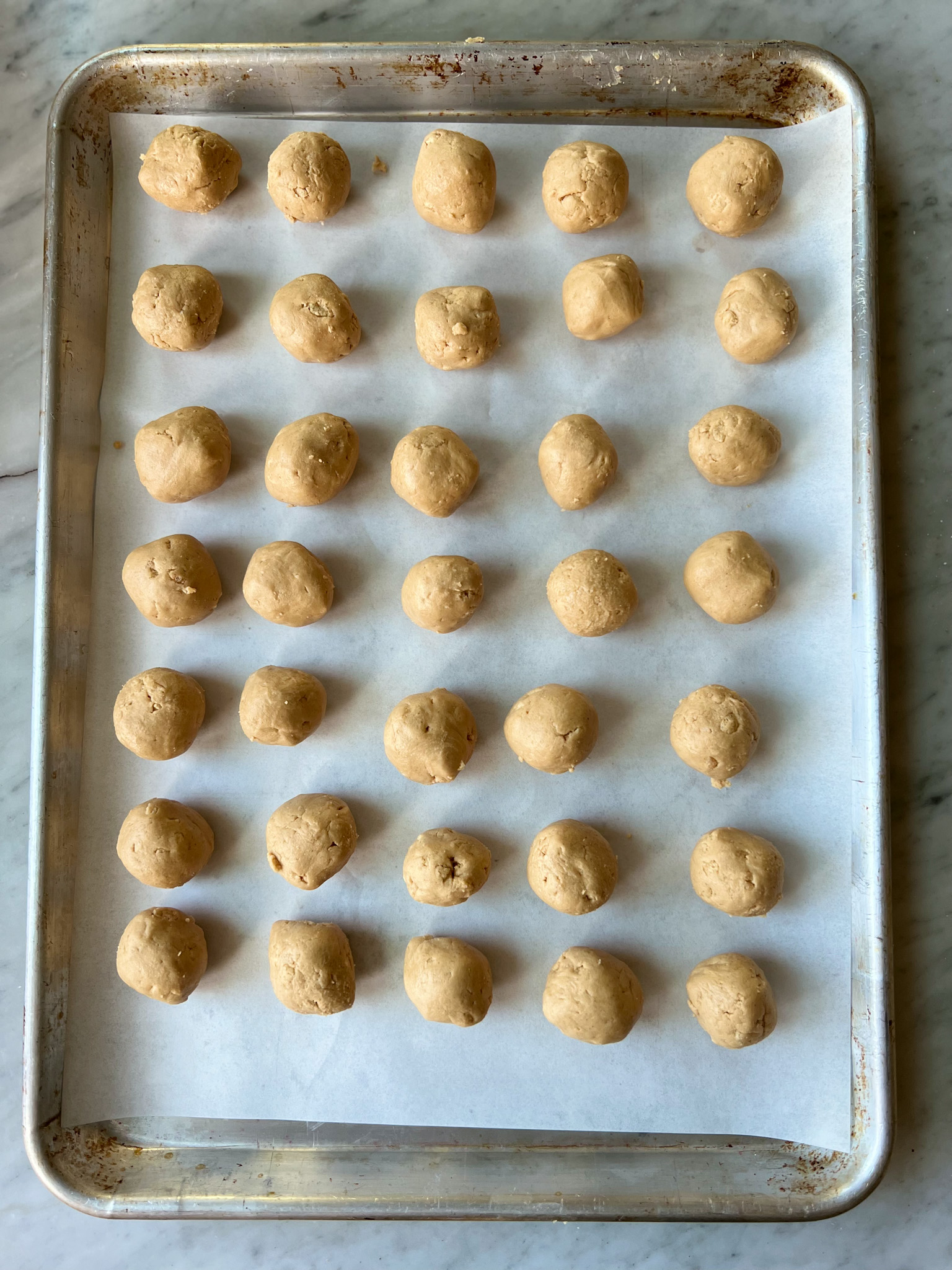 peanut butter balls rolled and on parchment on a sheet pan