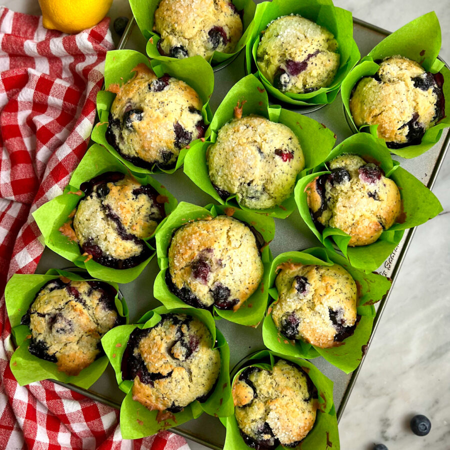 freshly baked lemon blueberry muffins with a red and white towel and a lemon and blueberries