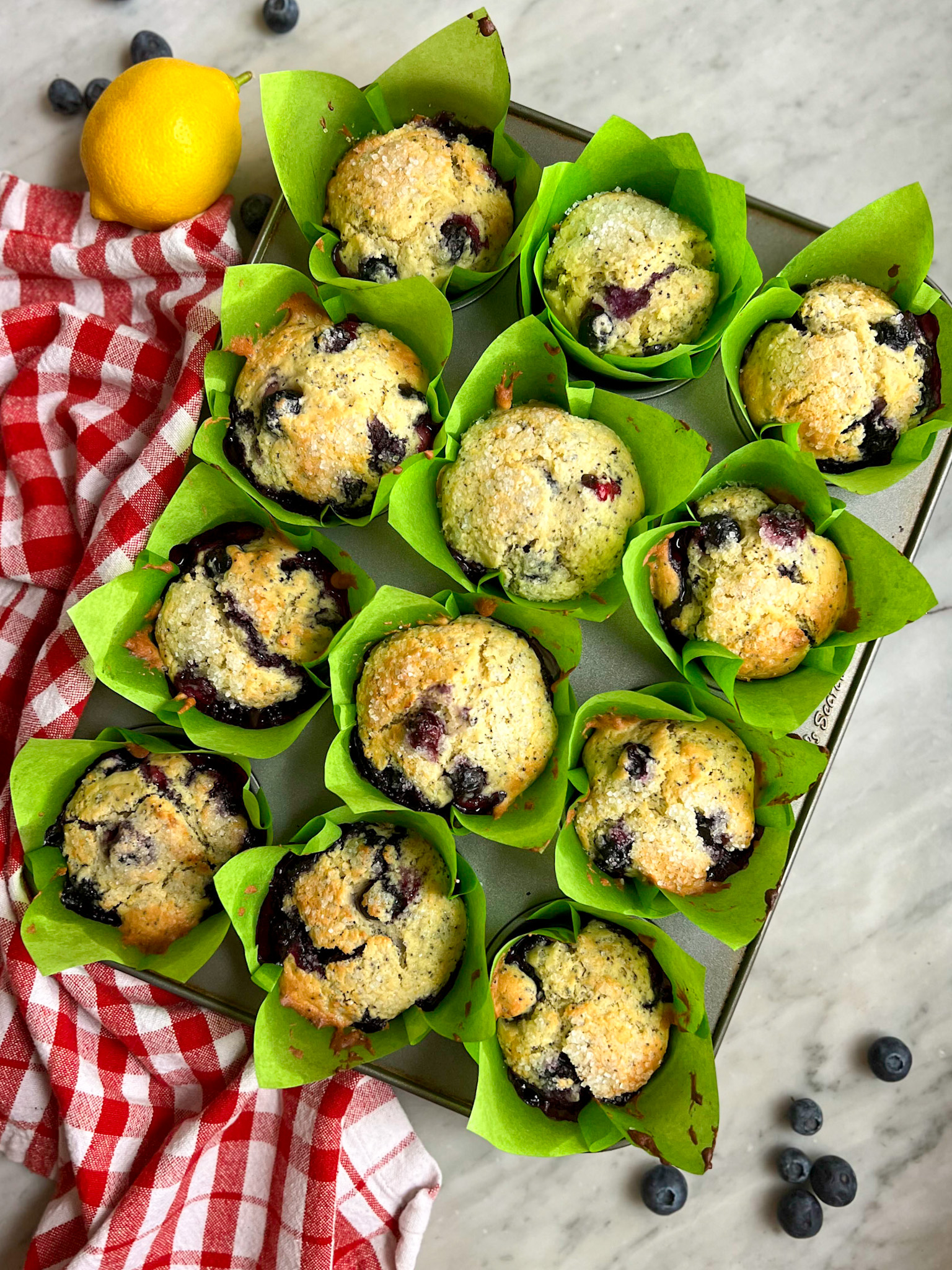 freshly baked lemon blueberry muffins with a red and white towel and a lemon and blueberries