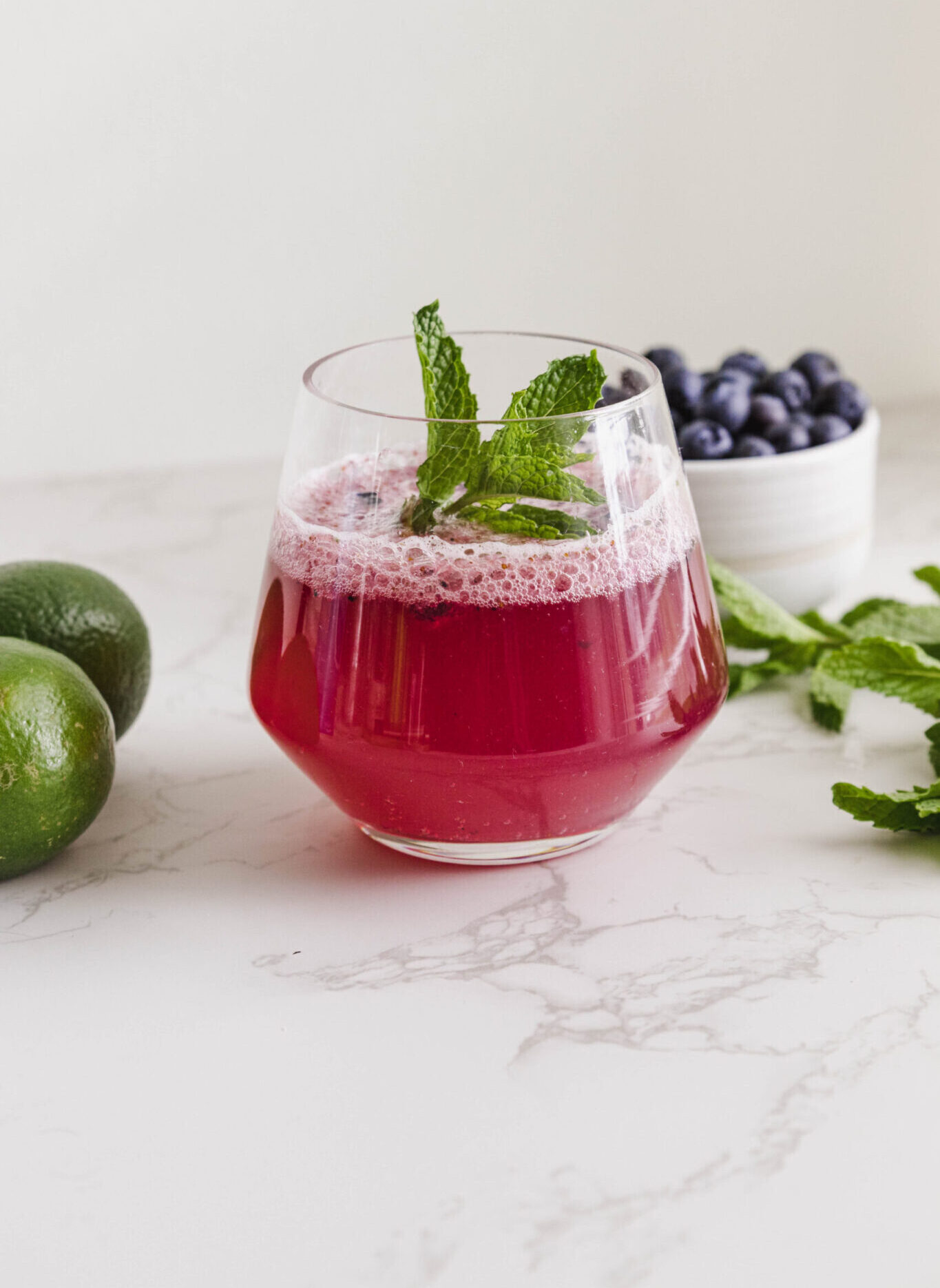 blueberry mocktail with mint in a glass and a bowl of blueberries and mint leaves and limes