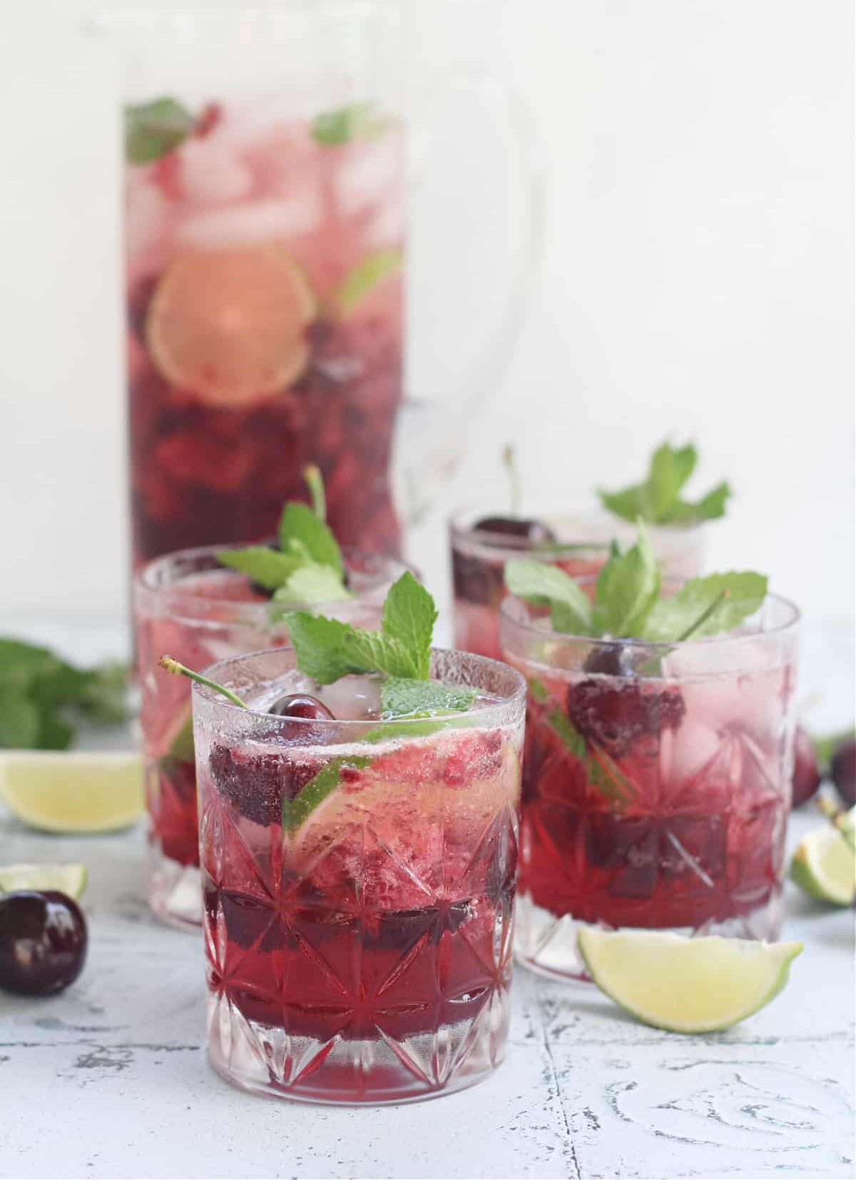 2 cherry mocktails with mint in a glass plus a pitcher