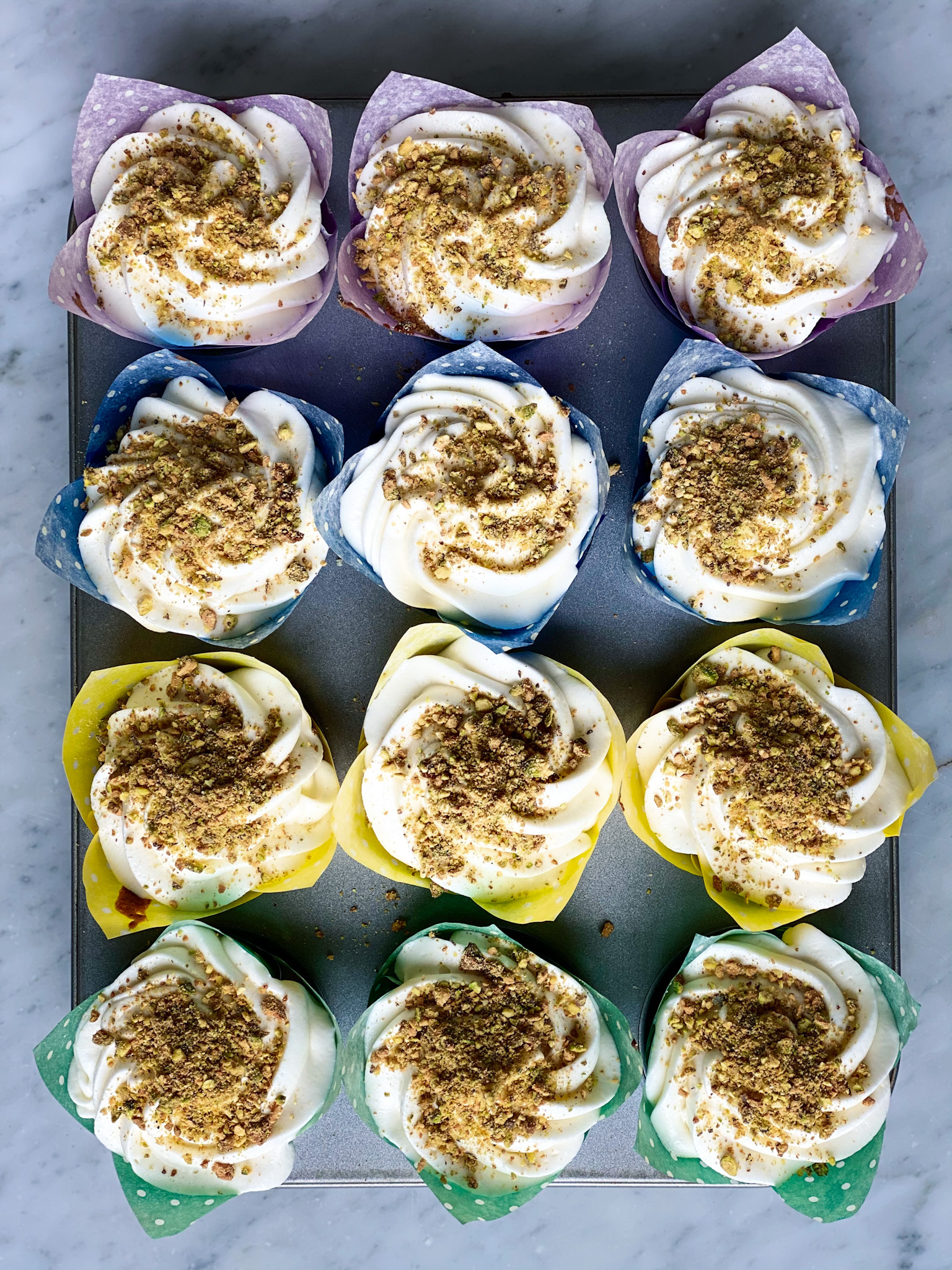 1 dozen pistachio cupcakes with cream cheese frosting and pistachios on top