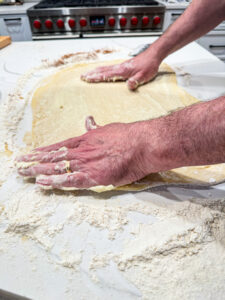 hands adding butter to dough for cinnamon rolls