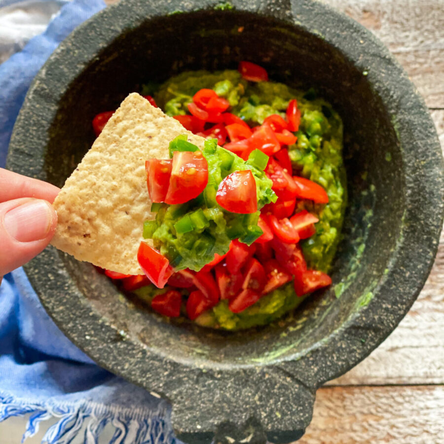 guacamole in a mocajete with a hand and a chip with some guac on it