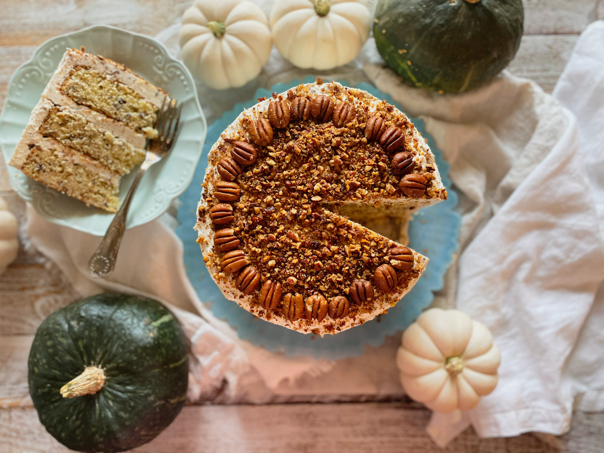 Butter pecan cake with a slice out on a plate and green and white pumpkins