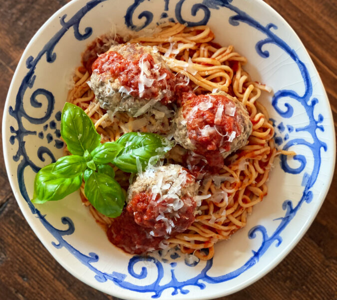 3 MEATBALLS on spaghetti and sauce in a blue and white bowl with basil