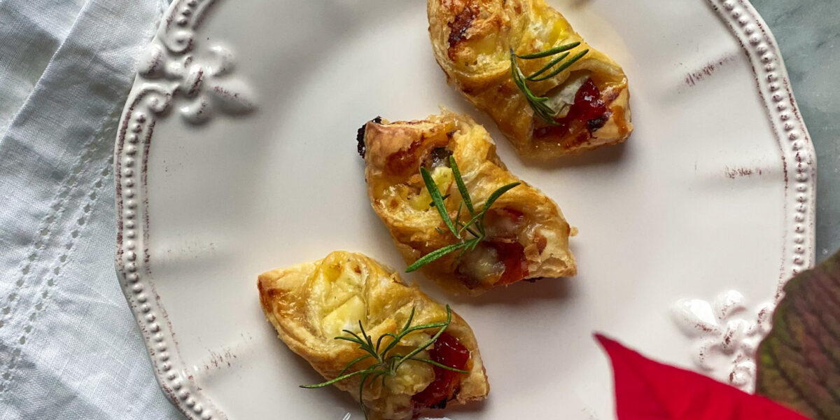 3 puff pastry wrapped brie, prosciutto, and pepper jelly bites, with a glass of champagne, with cranberries, and a poinsettia