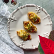 3 puff pastry wrapped brie, prosciutto, and pepper jelly bites, with a glass of champagne, with cranberries, and a poinsettia