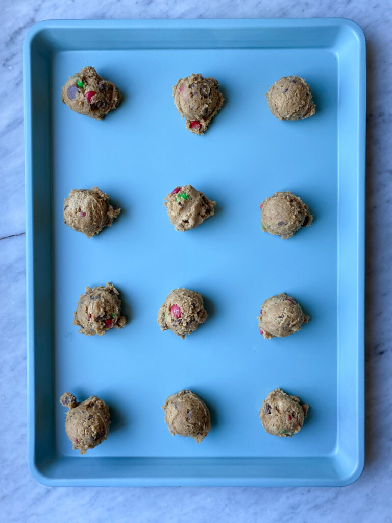Chocolate chip M&M cookie dough on a blue cookie pan