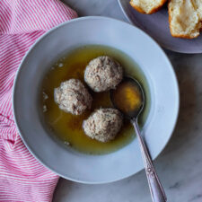 3 meatballs in broth with a plate of rolls