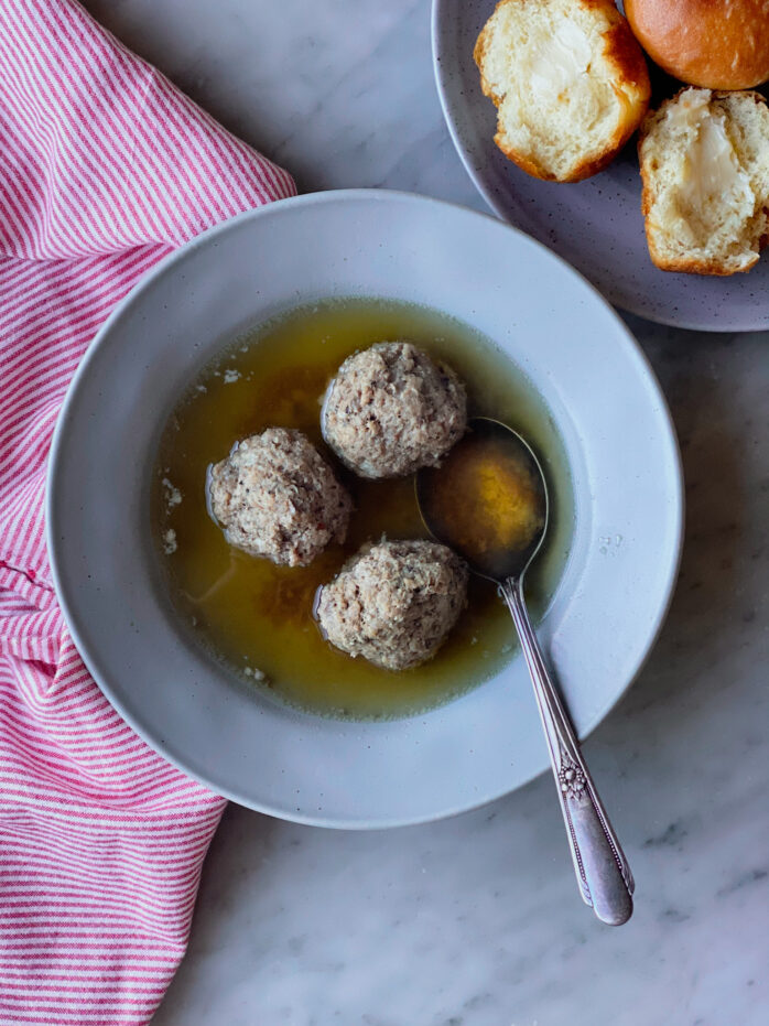 3 meatballs in broth with a plate of rolls