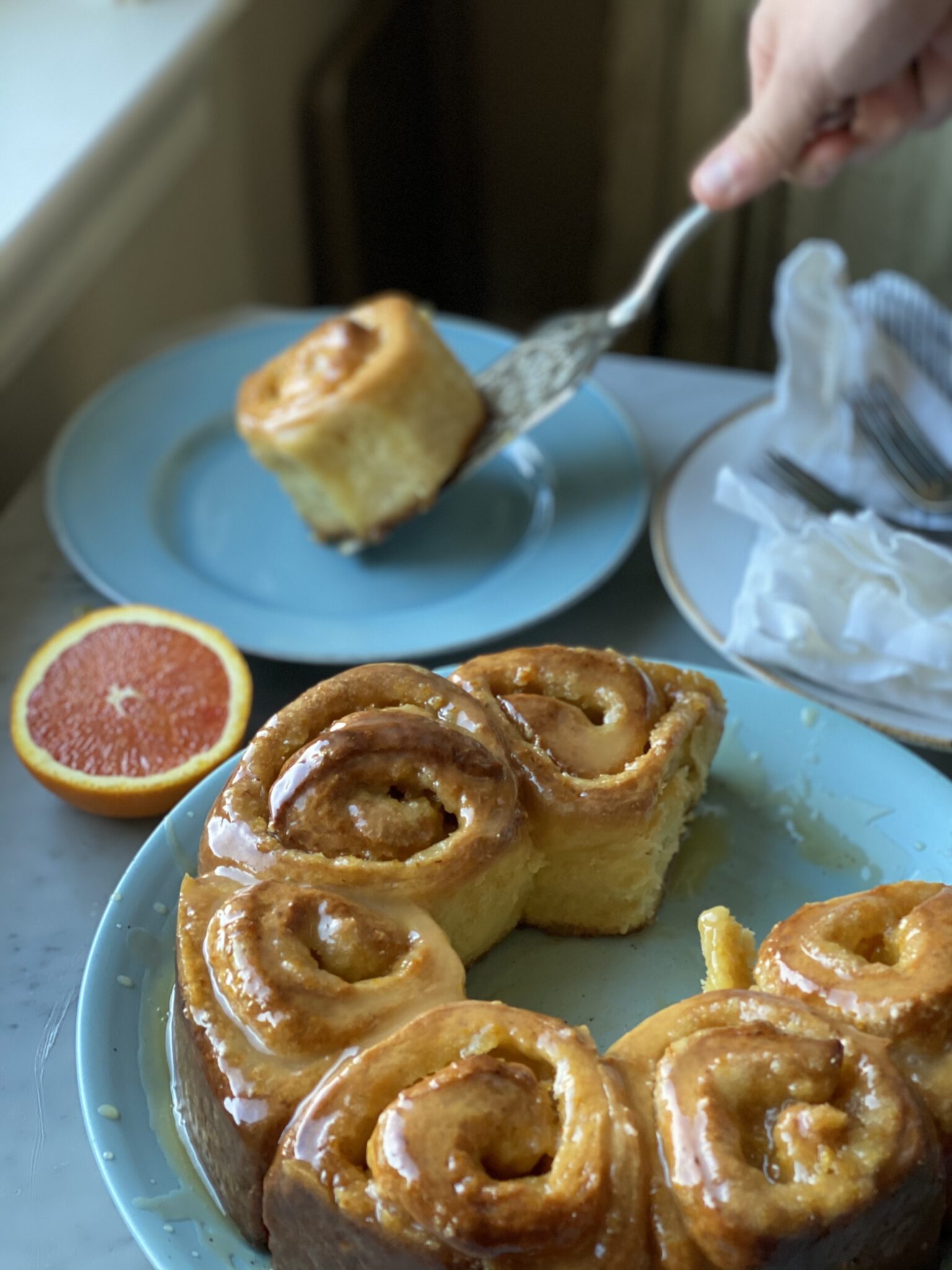 A roll being served and a plate of orange rolls and a half of orange