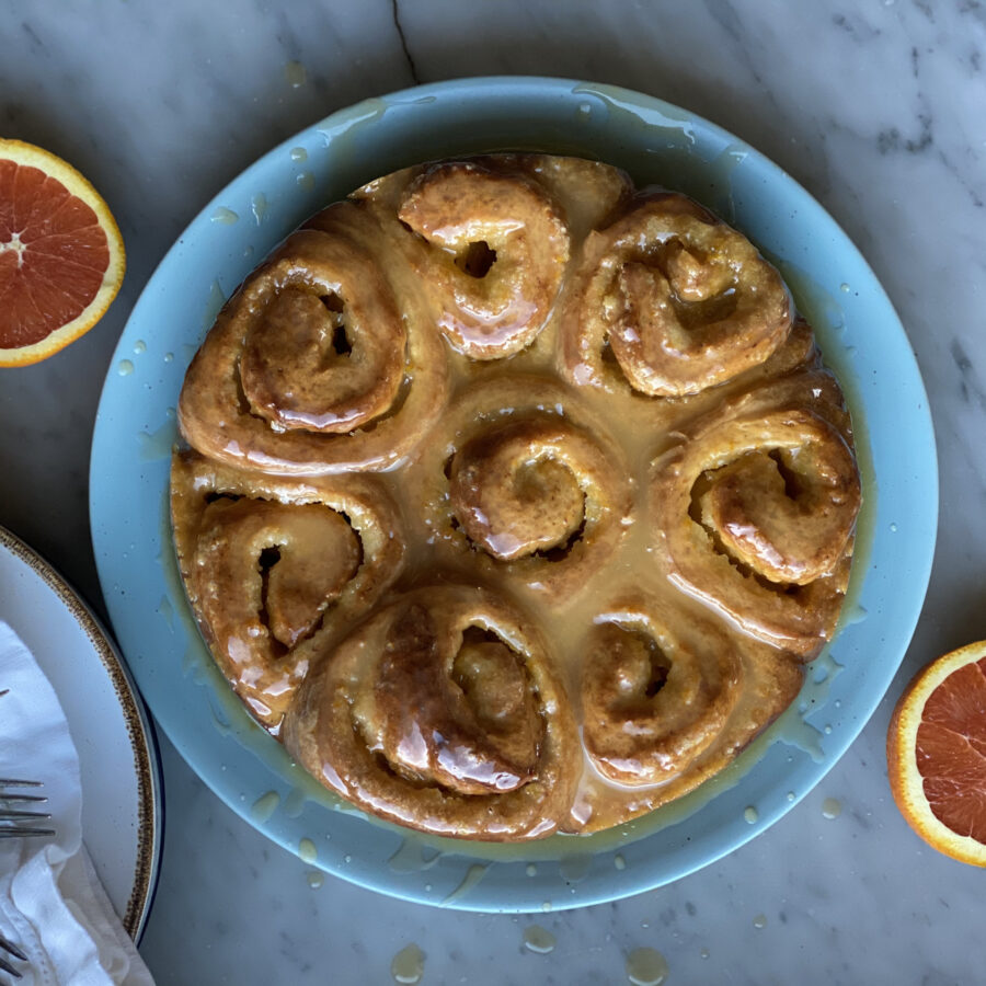 a plate of orange rolls and 2 oranges
