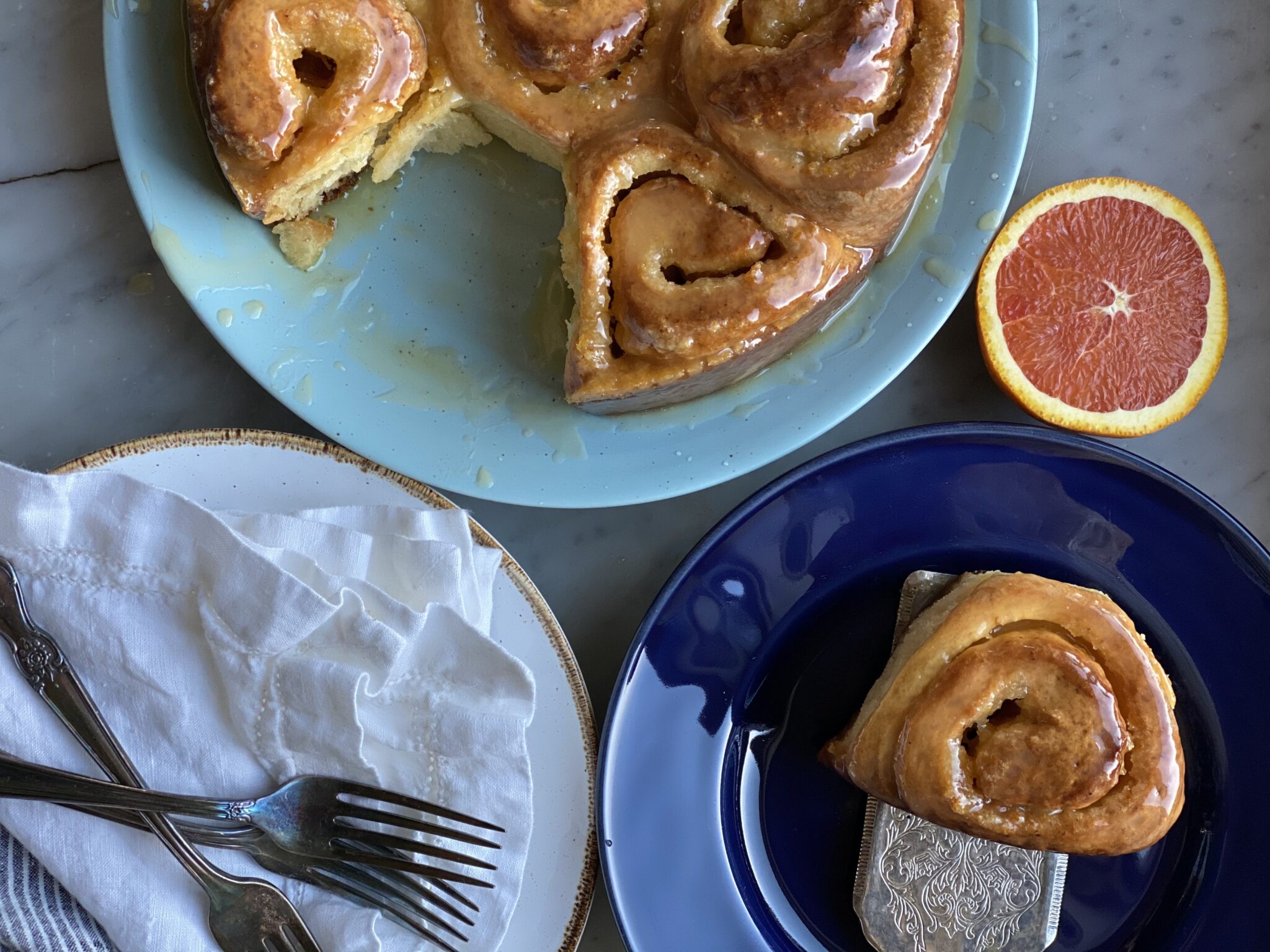 orange rolls on a plate with one on another plate with 2 forks and napkins and an orange