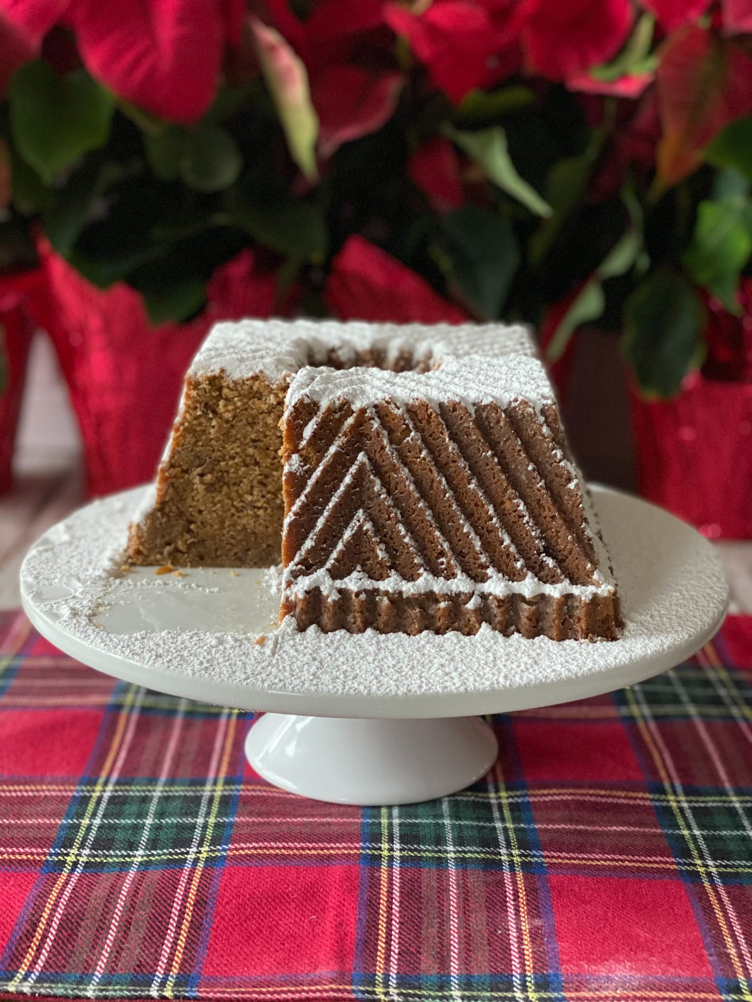 Bourbon butter pecan pound cake on a white cake stand with a cut out of it. Red flowers in backround