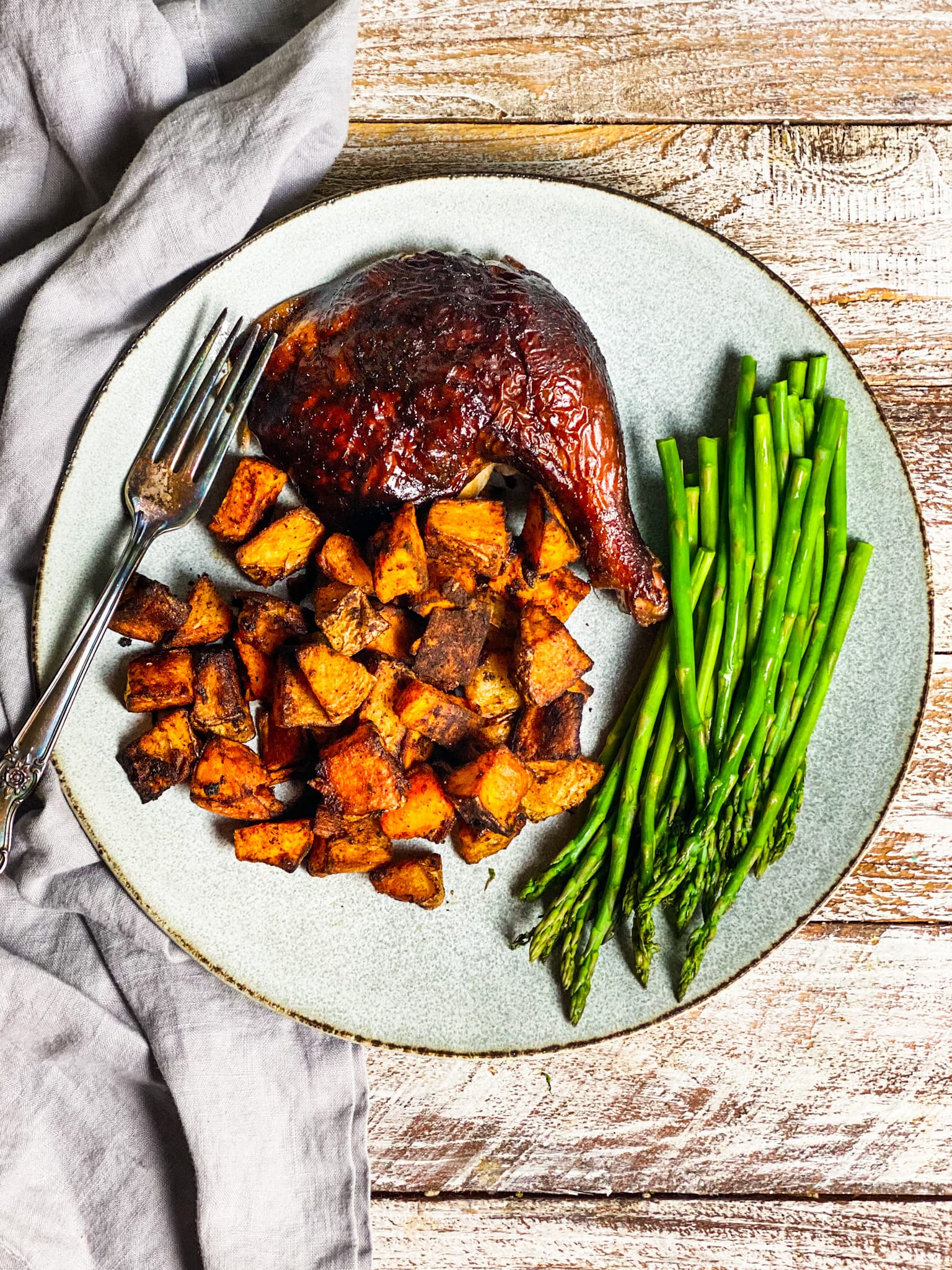 Smoked chicken quarter with roasted potatoes and asparagus on a plate with a fork and a napkin