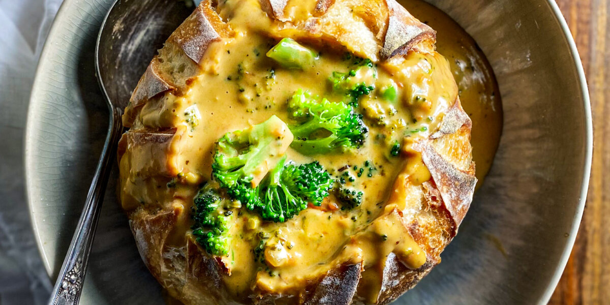 Broccoli Cheese soup in a sourdough bread bowl with a spoon and white napkin