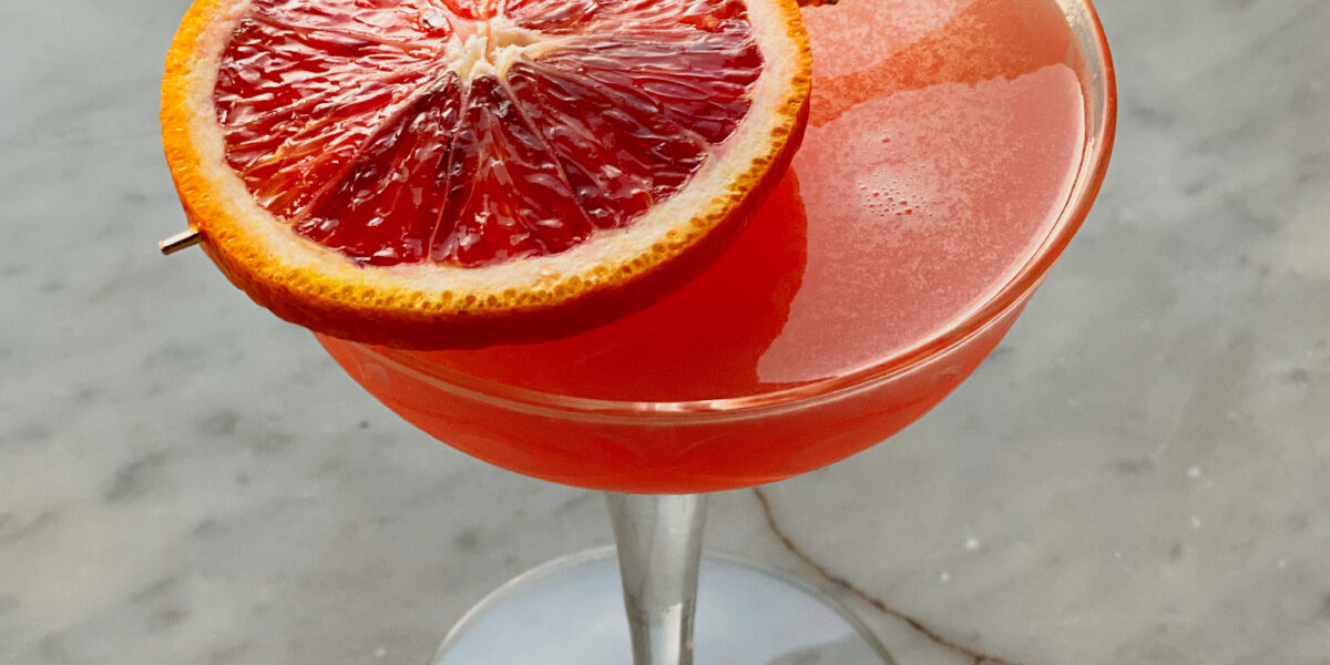citrus martini in a martini glass with a blood orange slice skewered on top