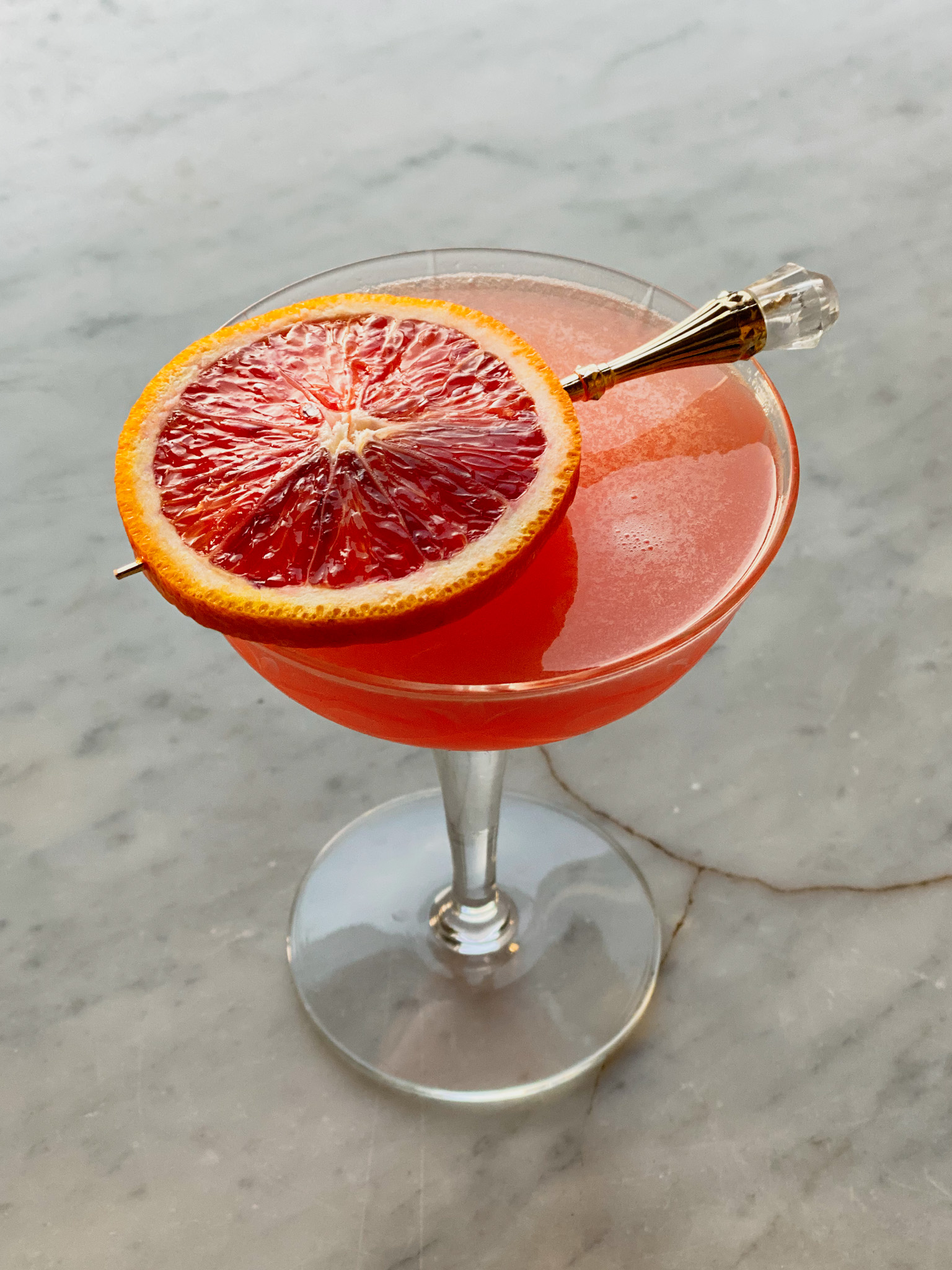 citrus martini in a martini glass with a blood orange slice skewered on top