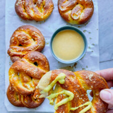 5 soft pretzels and cheese sauce and one pretzel with mustard and a bite taken out of it being held by a hand