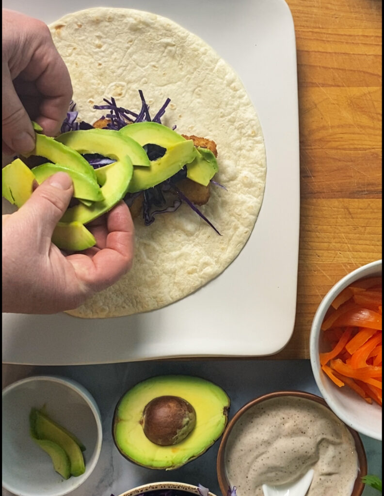 Hands adding avocado slices to the burrito