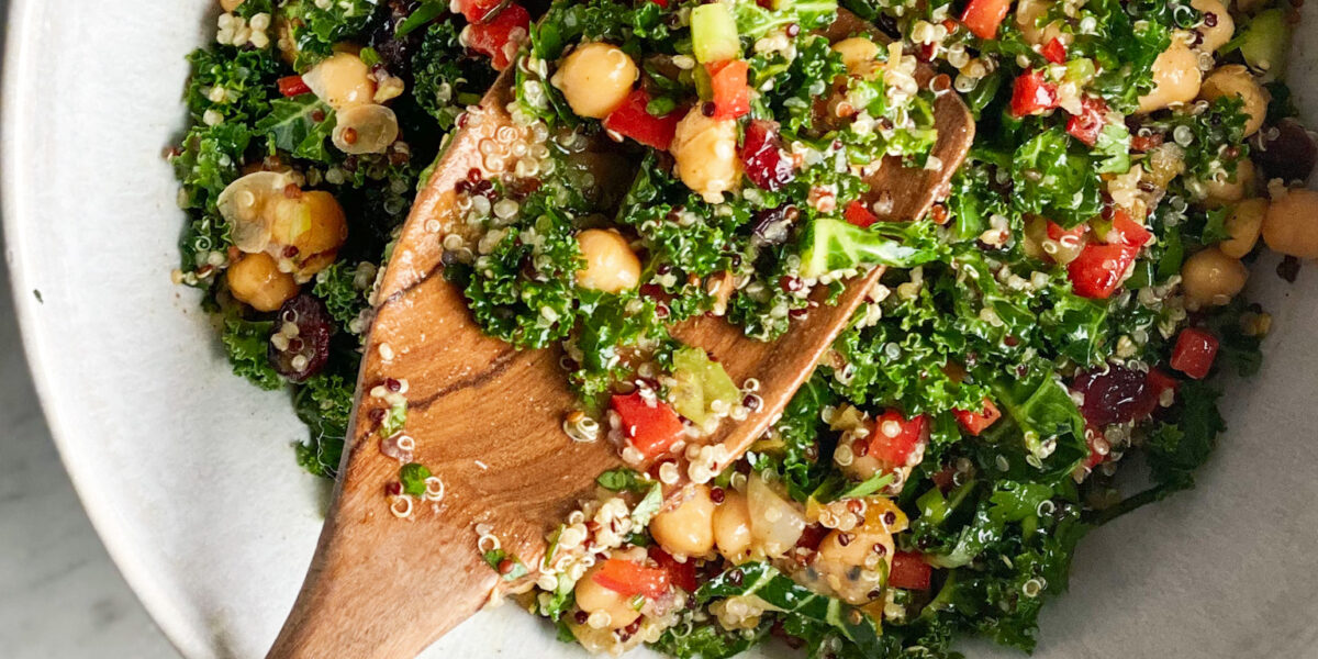 curried quinoa and kale salad in a white bowl with a wooden spoon and dried apricots
