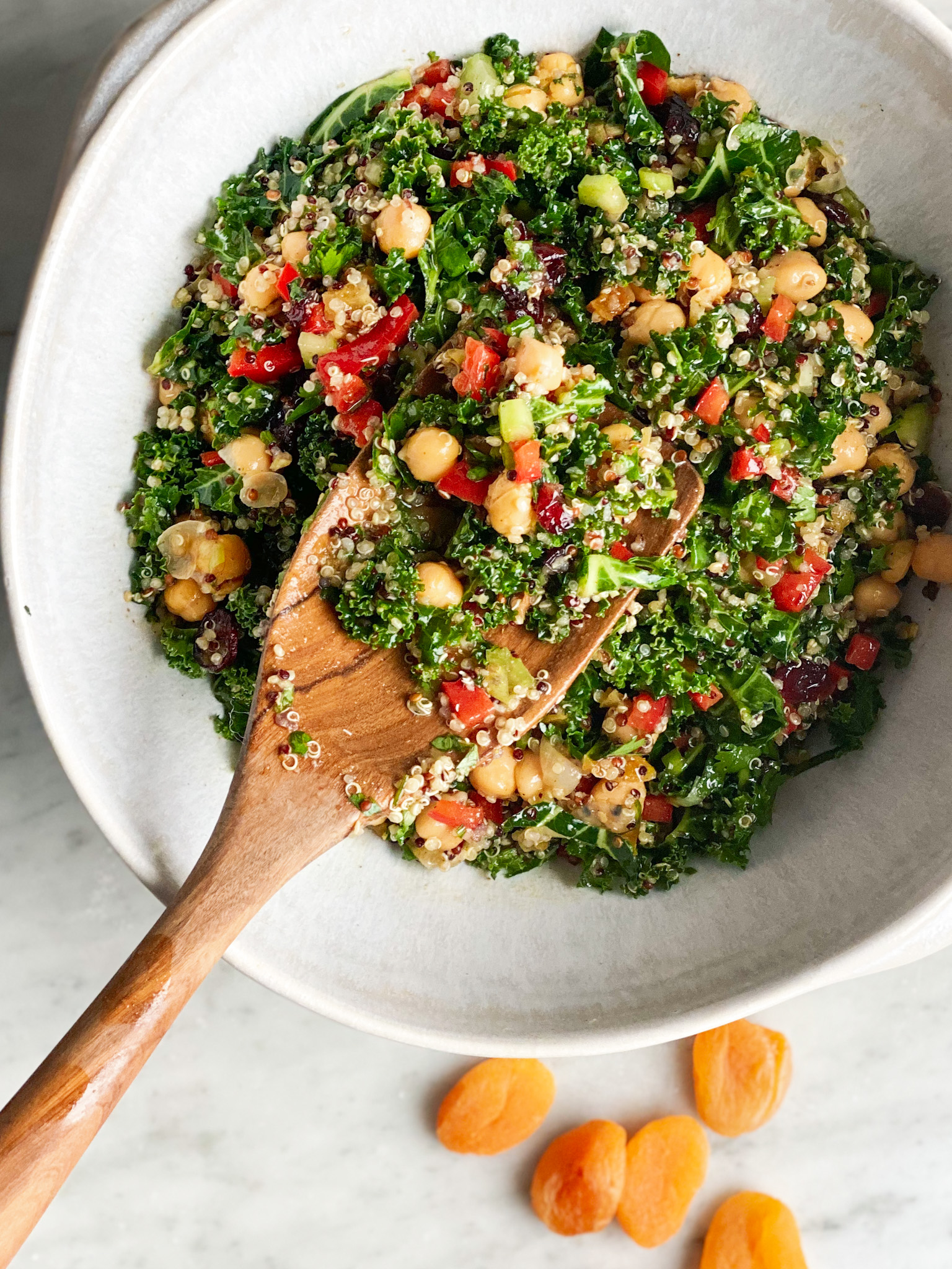 curried quinoa and kale salad in a white bowl with a wooden spoon and dried apricots