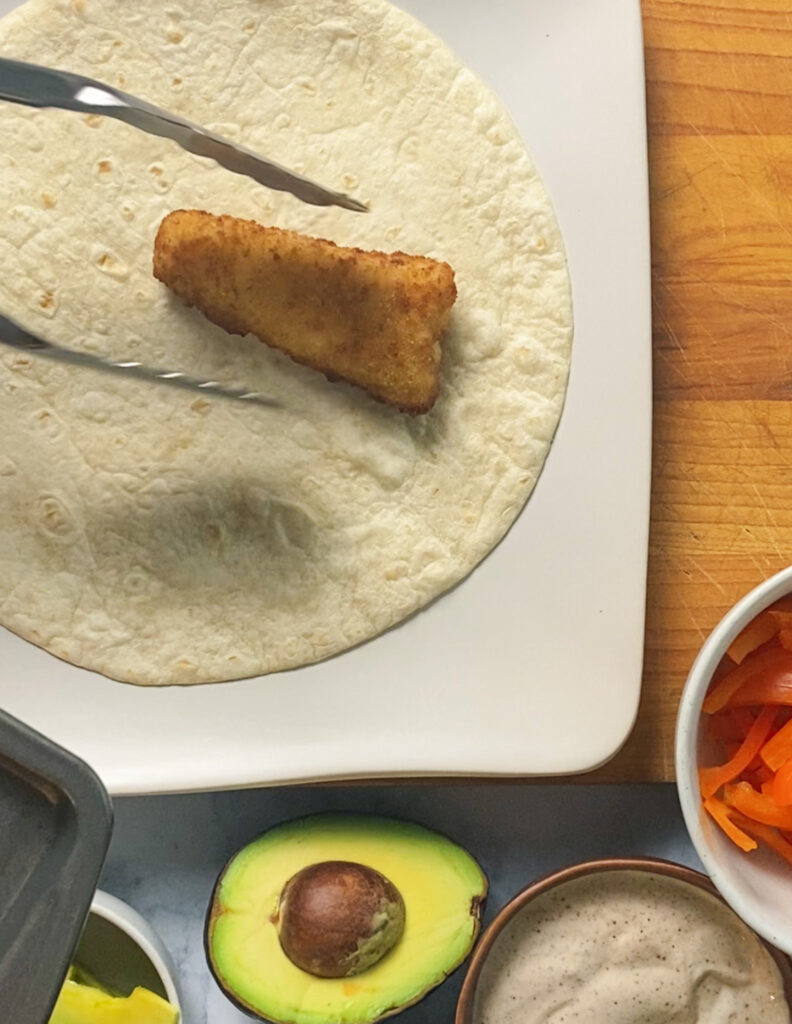 1 fish stick being added to a flour tortilla