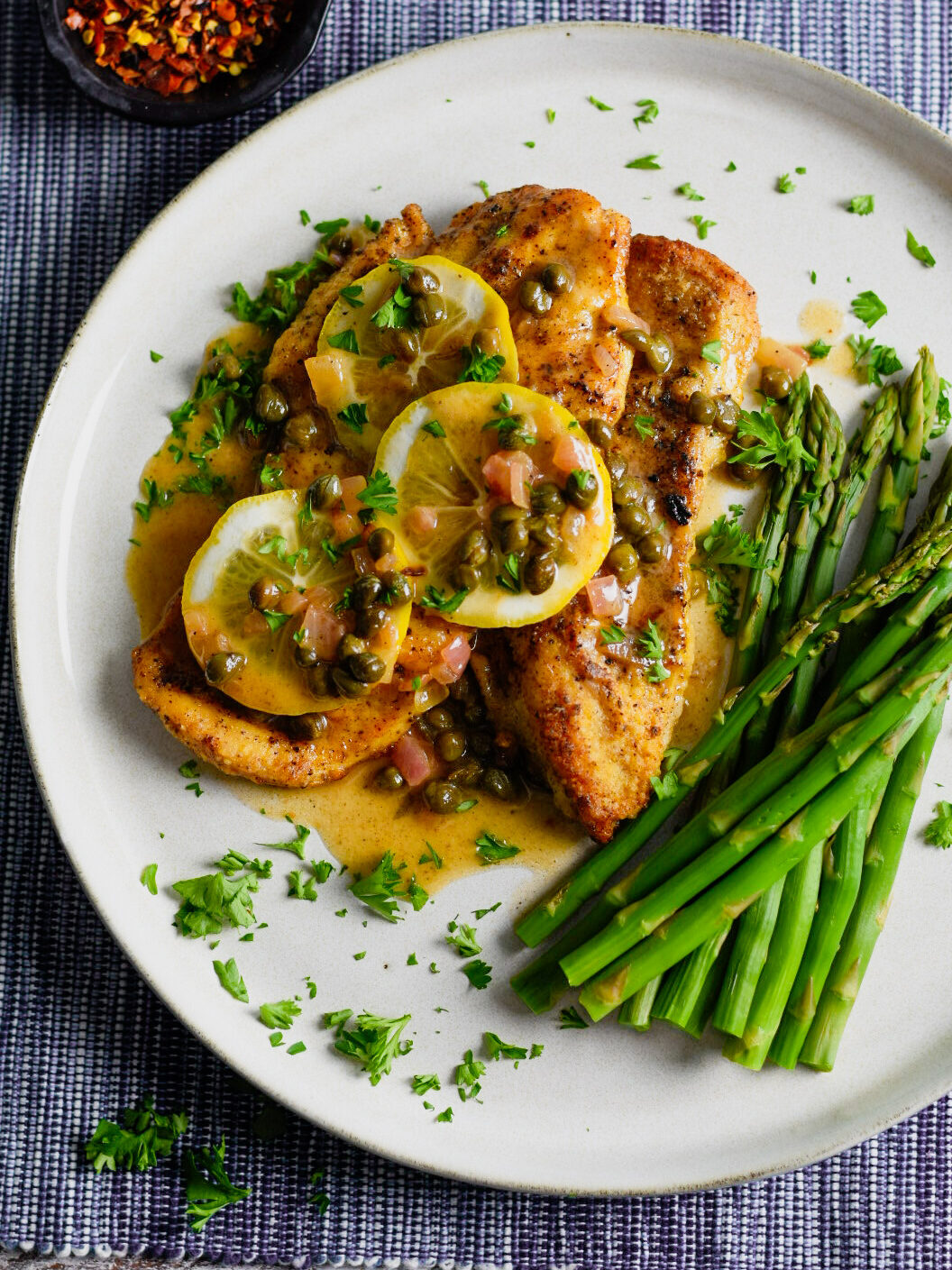 chicken piccata with lemons and asparagus on a white plate
