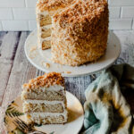 3 layer coconut cream cake with toasted coconut and a slice on a plate with a fork and a green nampkin