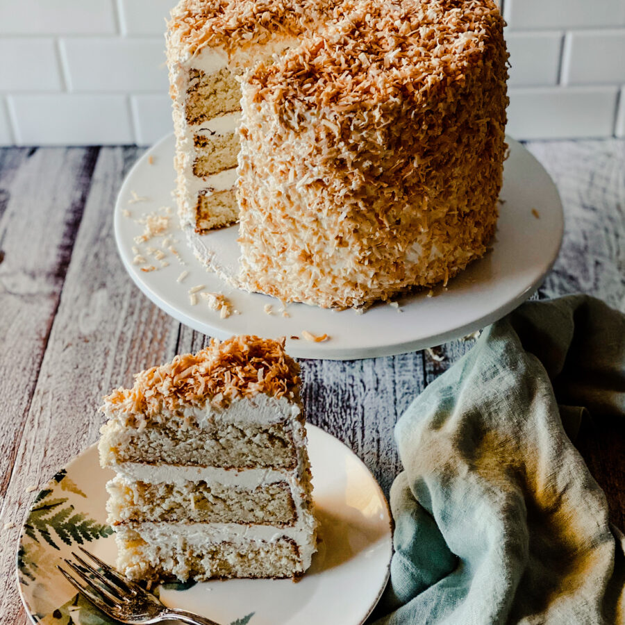 3 layer coconut cream cake with toasted coconut and a slice on a plate with a fork and a green nampkin