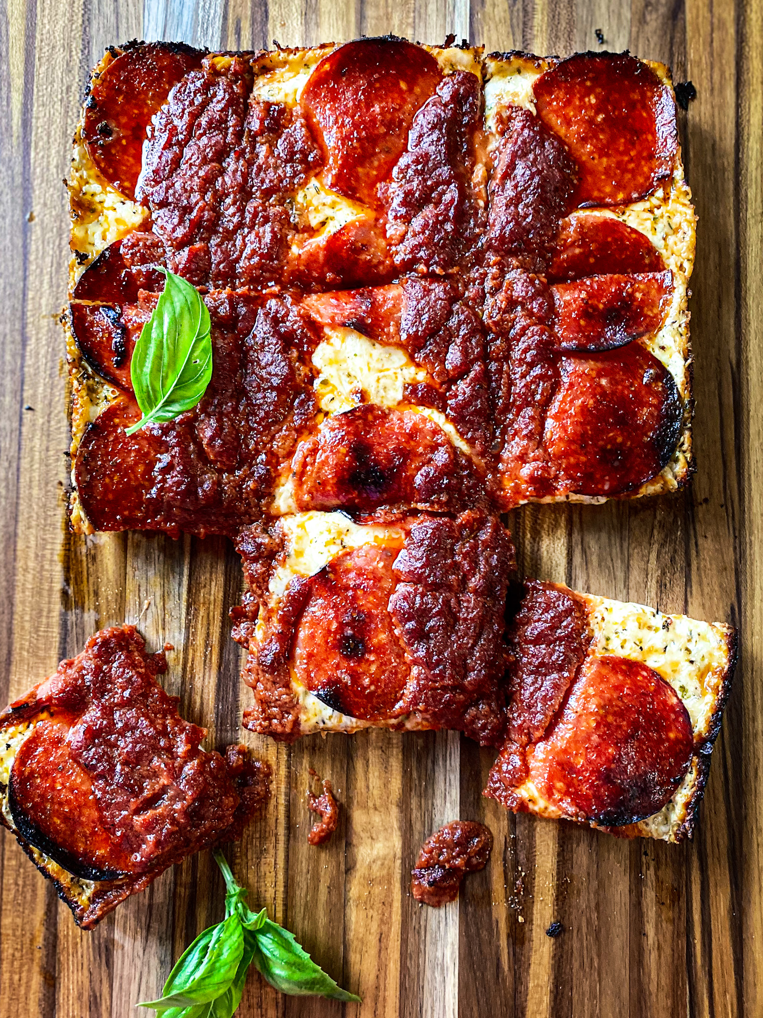 Detroit pepperoni pizza on a cutting board with basil