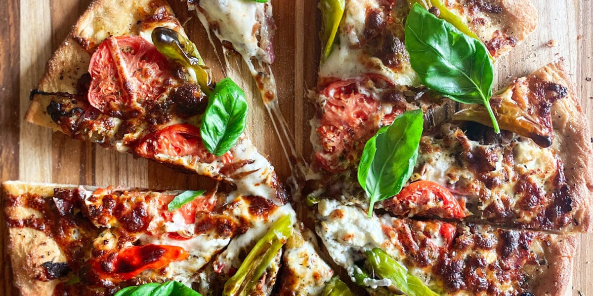 Pizza sliced with a piece out of it and basil leaves on top