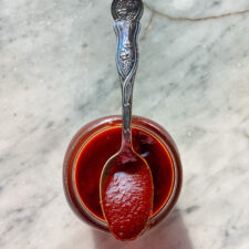 BBQ sauce in a spoon sitting on a mason jar of sauce