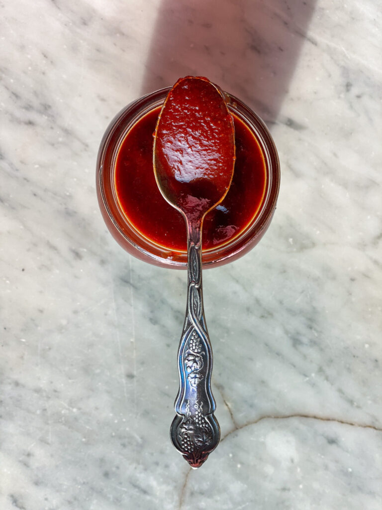 BBQ sauce in a spoon sitting on a mason jar of sauce