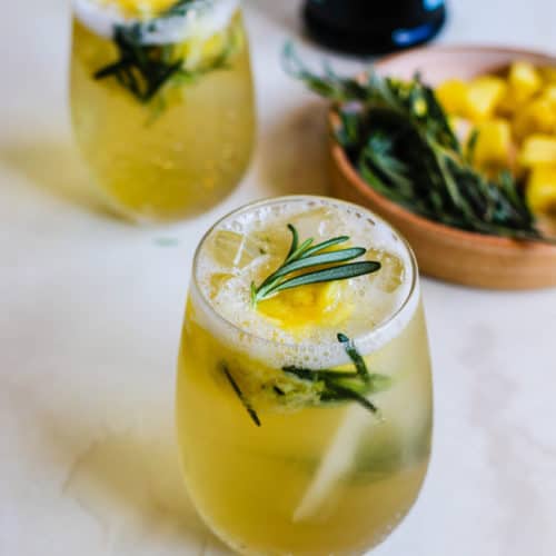 2 pinapple rosemary smashes with a tray of pineapple and rosemary