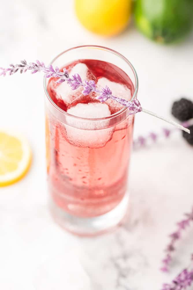 Purple rain cocktail in a clear glass with ice and a flower and lemon slice