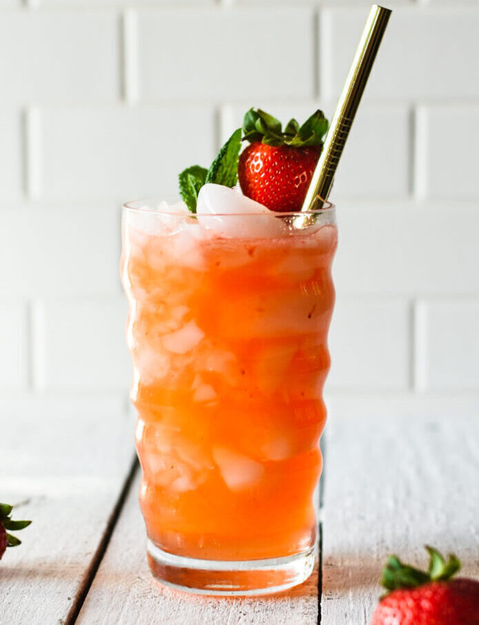Strawberry moscow mule over ice with a straw and strawberry and mint leaves on top