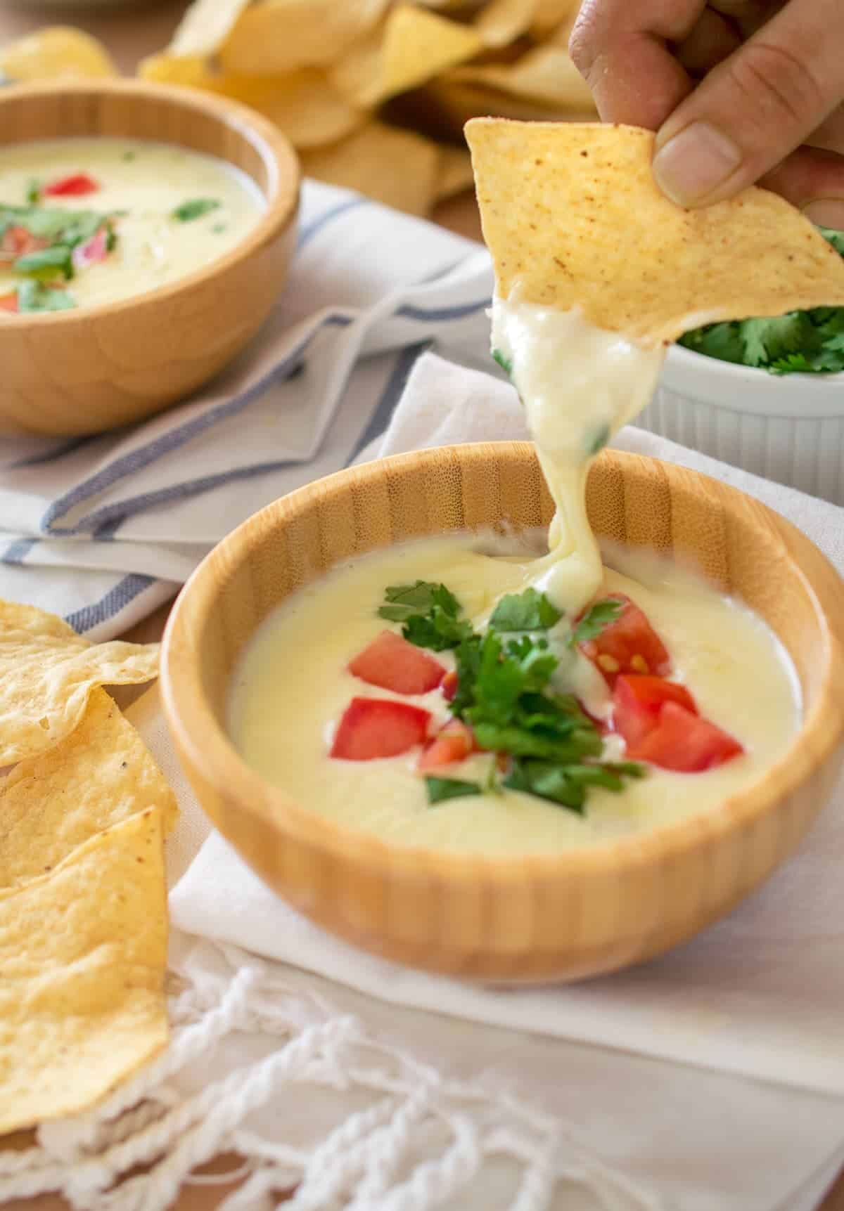 white cheese dip in a bowl with tomatoes and cilantro on top and a chip dipping in it