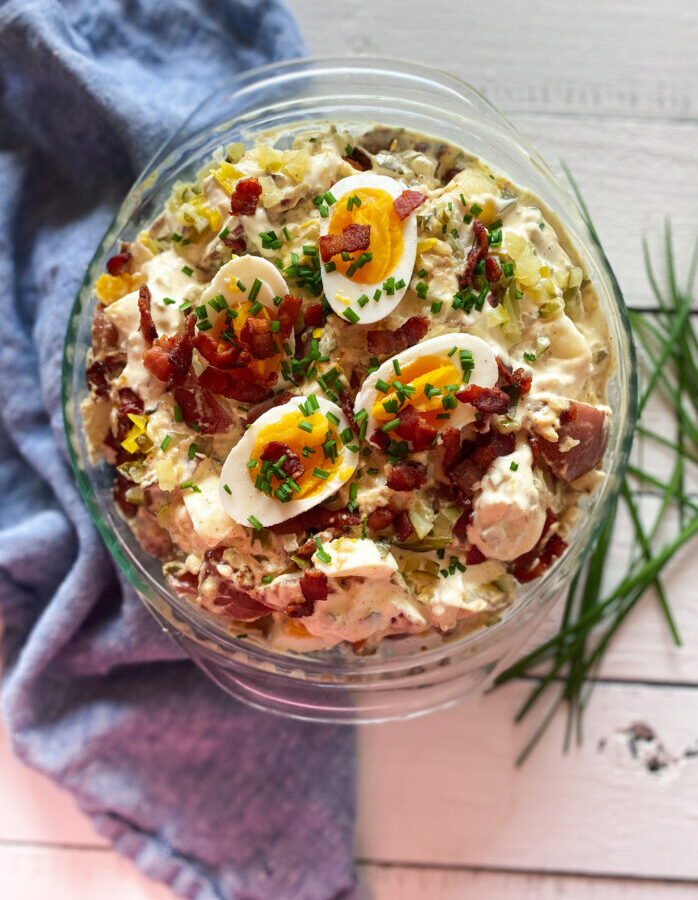 potato salad with bacon and eggs and chives in a glass bowl with a blue napkin