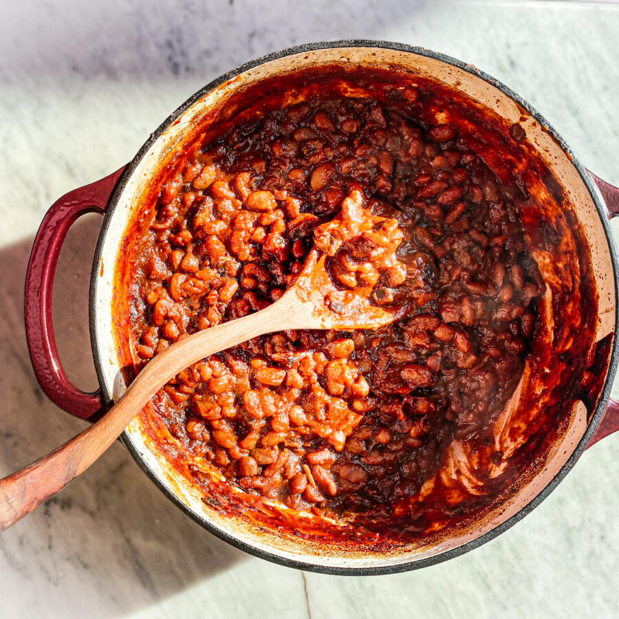 Baked beans in a cast iron dutch oven with a wooden spoon